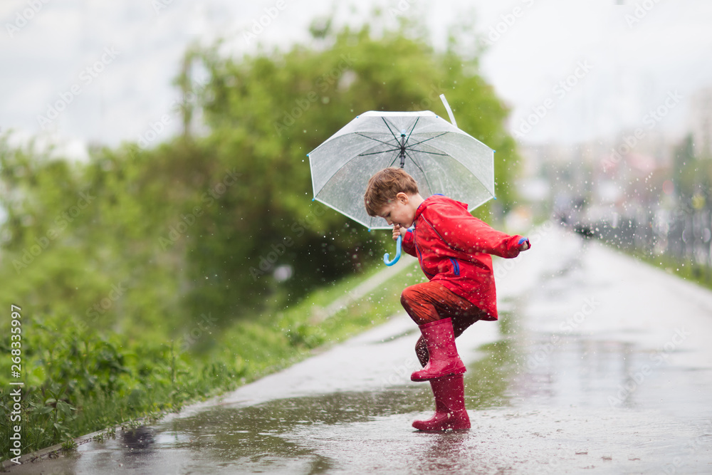 little child boy with an umbrella playing out in the rain in the summer outdoors - obrazy, fototapety, plakaty 