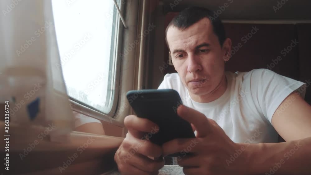 man businessman with smartphone travelling by train. man traveler is typing a internet web message in a train on the railway en route sits by the window of a carriage. slow lifestyle motion video