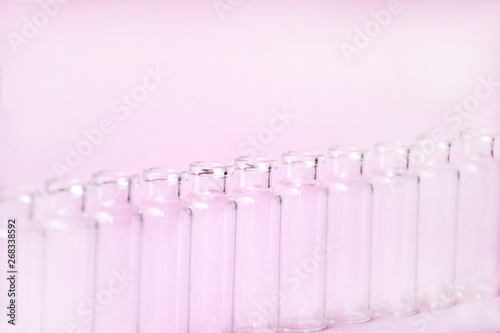 Empty glass medical vials, ampoules in a row on a light pink background with space for text. Glass medical bottles with selective focus. Vaccines, Medicine, Laboratory, Immunization concept.