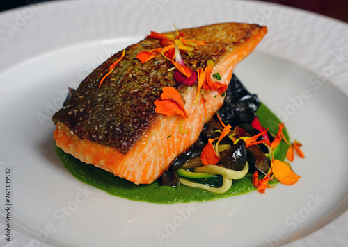 Gourmet dish of seared salmon trout on green pea puree with edible flowers photo