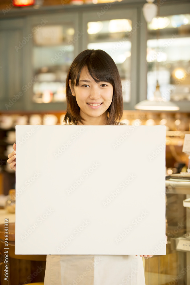 メッセージボードを持ち微笑むカフェの店員
