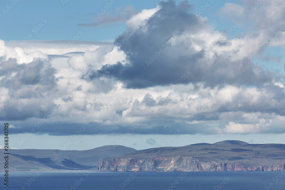Orney cliffs with dramatic sky seen from John o'Groats over Atlantic ocean.