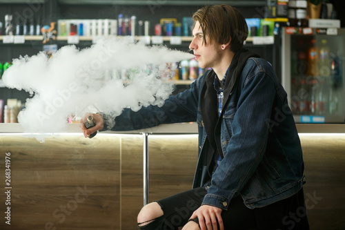 Vape teenager. Portrait of young handsome guy smoking an electronic cigarette in the vape bar. Bad habit that is harmful to health. Vaping activity.