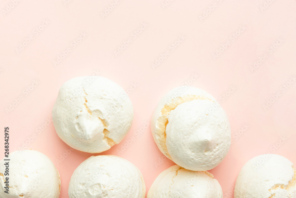 Home baked meringue cookies scattered on light pink background. French Italian Swiss cuisine desserts. Airy elegant style. Recipe poster template