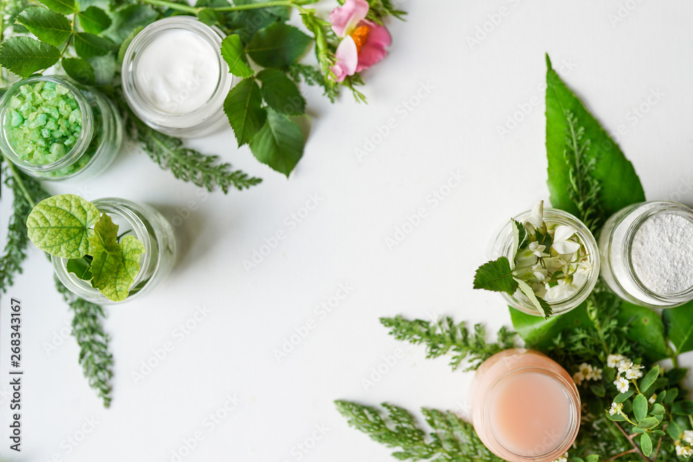 facial body cosmetic products, leaves and flowers blossom on white desktop background whith copy space. spring skin care layout, top view, flat lay. Natural beauty product concept. - obrazy, fototapety, plakaty 