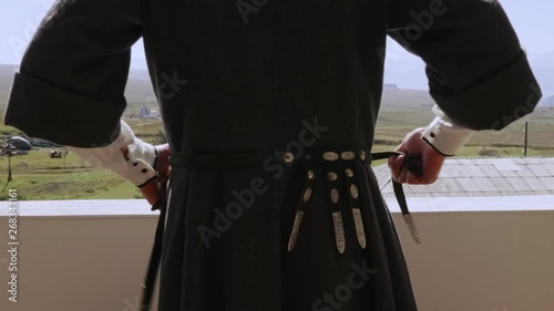 guy in circassian tightens traditional dagger leather belt standing on balcony of pictorial highland close back view photo