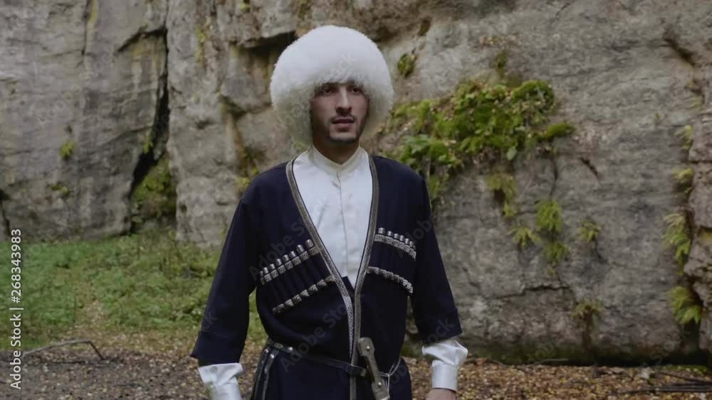 serious man with black beard in white Dagestan fur hat papakha and  circassian coat takes dagger out of scabbard in gorge Stock Video | Adobe  Stock