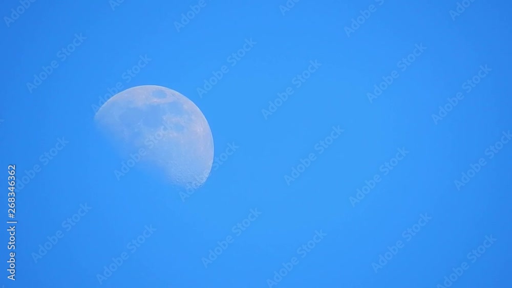 Glowing details on moons surface on blue sky morning view. Shadowy lower half of moons surface hidden. Glowing details on moons surface on blue sky morning view. Shadowy lower half of moons surface hidden.
