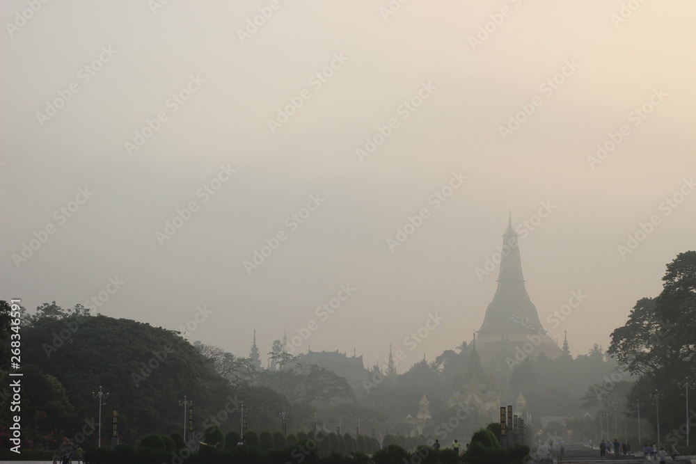 early morning views from a public park looking at the sun rising over Shwedagon pagoda, a large Buddhist monument in the centre of Yangon, Myanmar, Southeast Asia