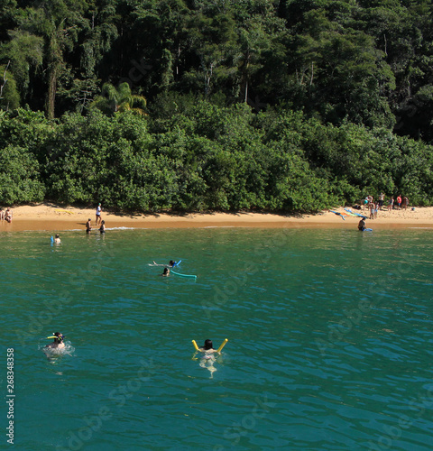 The people is in the beach. Some of them are walking in the sand and others are in the water. 