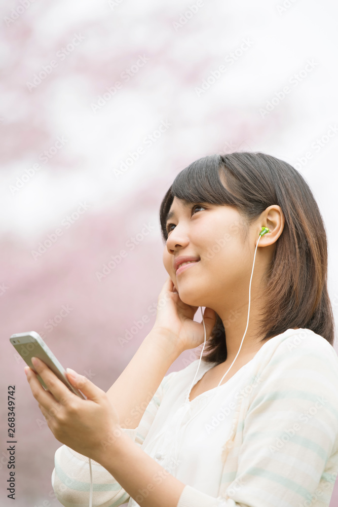 桜の前で音楽を聴く女性