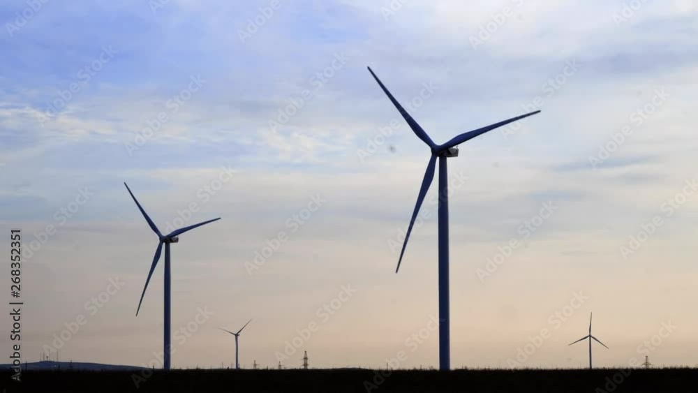 Evening silhouette of windmills with sun setting in background on a cloudy blue sky. These clean energy generating wind farms are densely populated in the state. Evening silhouette of windmills with sun setting in background on a cloudy blue sky. These clean energy generating wind farms are densely populated in the state.