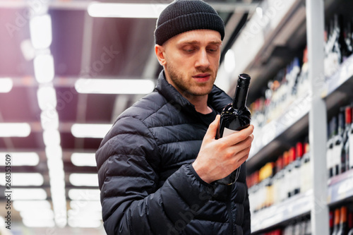 Young handsome man choosing wine in supermarket. Matter of wine choice.