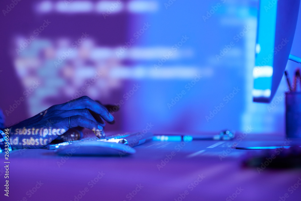 Close-up of young developer sitting at office desk and typing on computer keyboard in dark office Close-up of young developer sitting at office desk and typing on computer keyboard in dark office