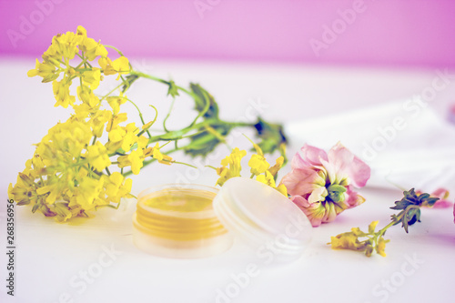  cosmetic oil for the face in a transparent jar with a lid  near wildflowers  twigs  white napkins  pink petals on a white background. Top view 