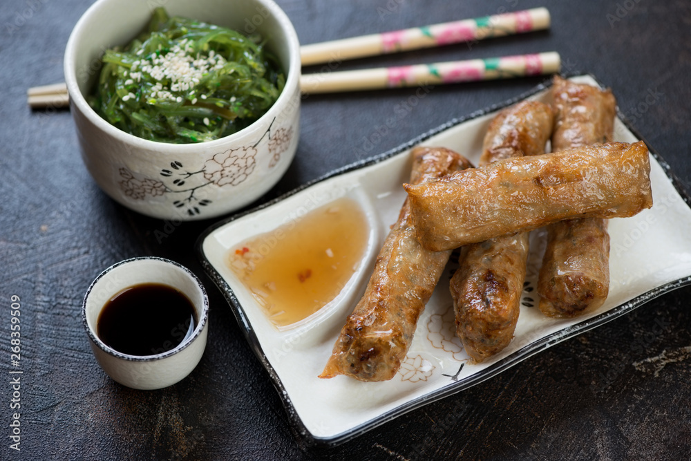 Traditional vietnamese fried spring rolls or nems with dips and seaweed salad, studio shot
