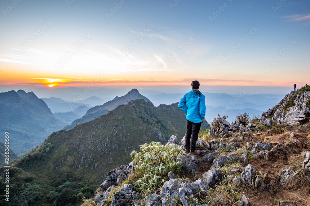 Obraz premium Man stand back to clear sky Cloud wait for sunset at top of wildlife sanctuary name Doi Luang Chiang Dao, Thailand with Shadow of mountain layer and sun ray.