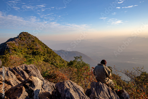 Man sitting back to clear sky Cloud wait for sunset at top of wildlife sanctuary name Doi Luang Chiang Dao, Thailand with Shadow of mountain layer and sun ray.