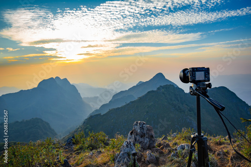 Tripod and Camera on shooting timelap of Golden sunset sky cloud at wildlife sanctuary name Doi Luang Chiang Dao, Thailand with Shadow of mountain layer and sun ray.