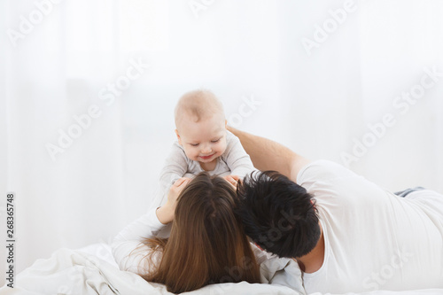 Family weekend together, lazy shining morning, cozy and warm photo. Playful parents holding their little cute baby boy over itself above. Mom and dad making kid smiling. Copyspace and Side view