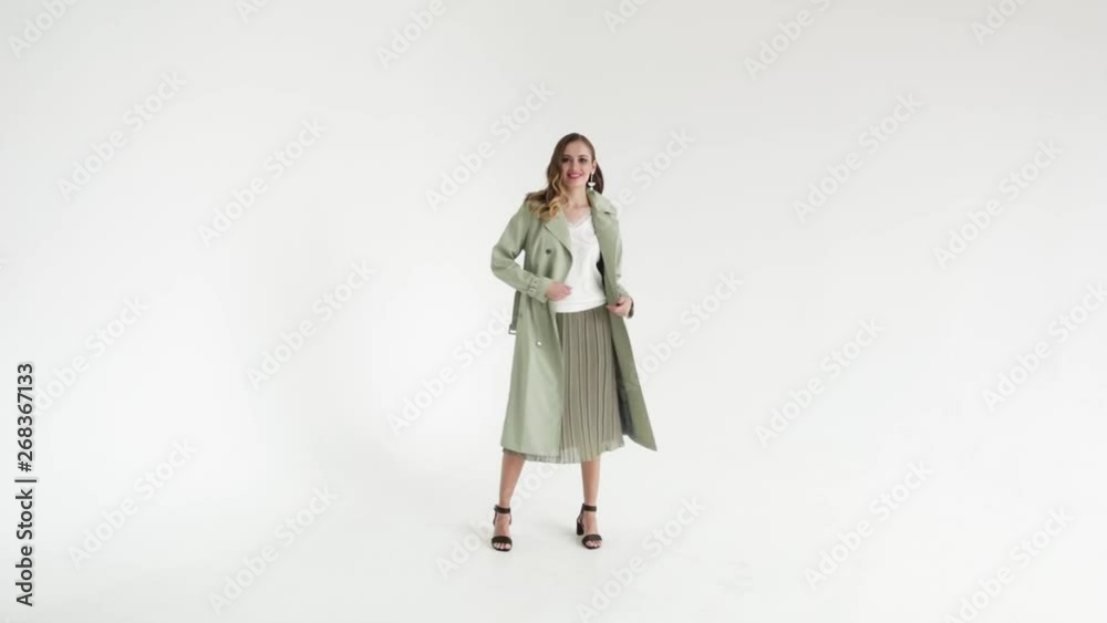 Elegant girl in an unbuttoned beige cloak, on a white background, the model poses, the girl unbuttoned his clothing, slow motion Elegant girl in an unbuttoned beige cloak, on a white background, the model poses, the girl unbuttoned his clothing, slow motion