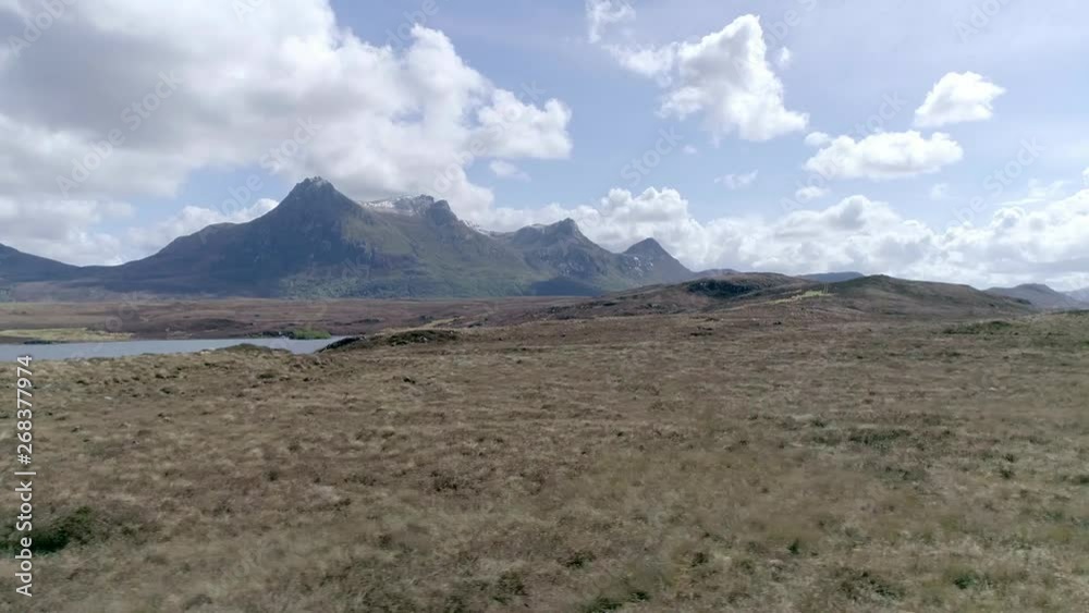 Left dolly move across rugged Scottish highland terrain, green, brown, grassy marsh meadow landscape under Ben Loyal mountain range summit along distant horizon. Left dolly move across rugged Scottish highland terrain, green, brown, grassy marsh meadow landscape under Ben Loyal mountain range summit along distant horizon.