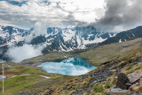 Turquoise mountain lake with snowy peaks and clouds in Italian Alps