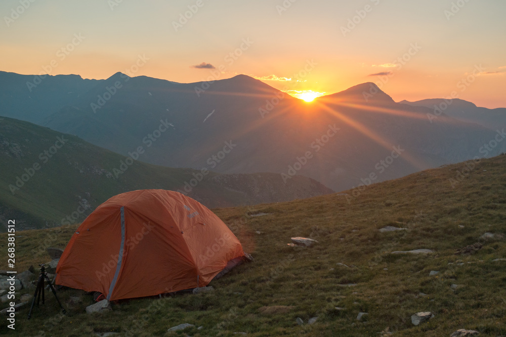 Zoom view of orange tent at sunrise with mountain background and sun