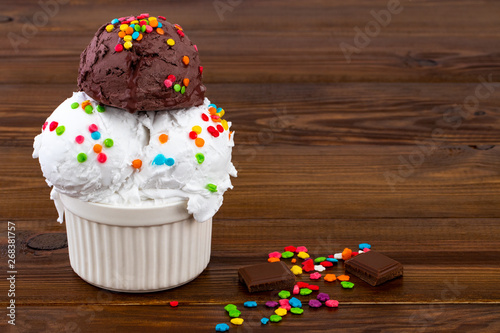 plate of vanill aand and chocolate ice cream scoop swith sprinkles and waffle cones on wooden background with copy space photo