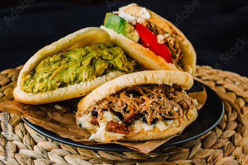 Venezuelan arepas on a black background, made with maize and filled with avocado, tomato, meat, cheese and black beans photo