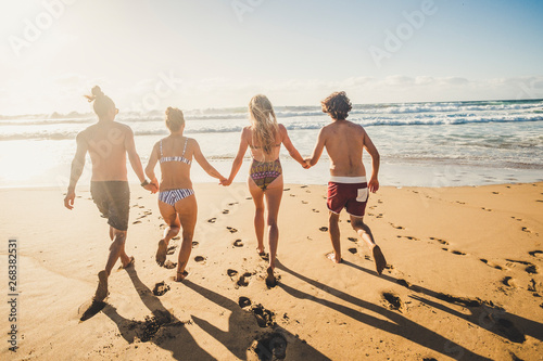 Group of young people friend have fun at the beach in summer holiday vacation running from sand to sea water together in friendship - youthful happy couples enjoy the sunny day with ocean