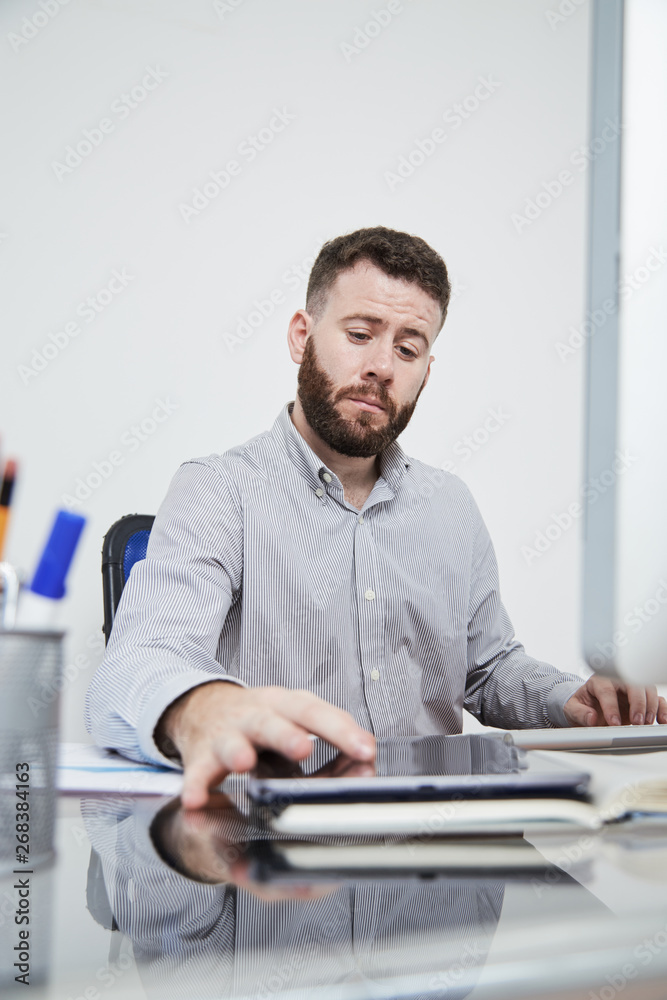 Fototapeta premium Bearded office manager sitting at office desk touching display of tablet pc and reading online message