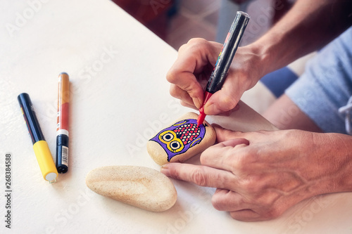 Hands of a woman painting an owl figure on a stone with an acrylic pen. Stone painting handicraft. photo