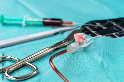 Scalpel, syringe, cannula and pair of scissors on green gauze with hole over the keyboard photo