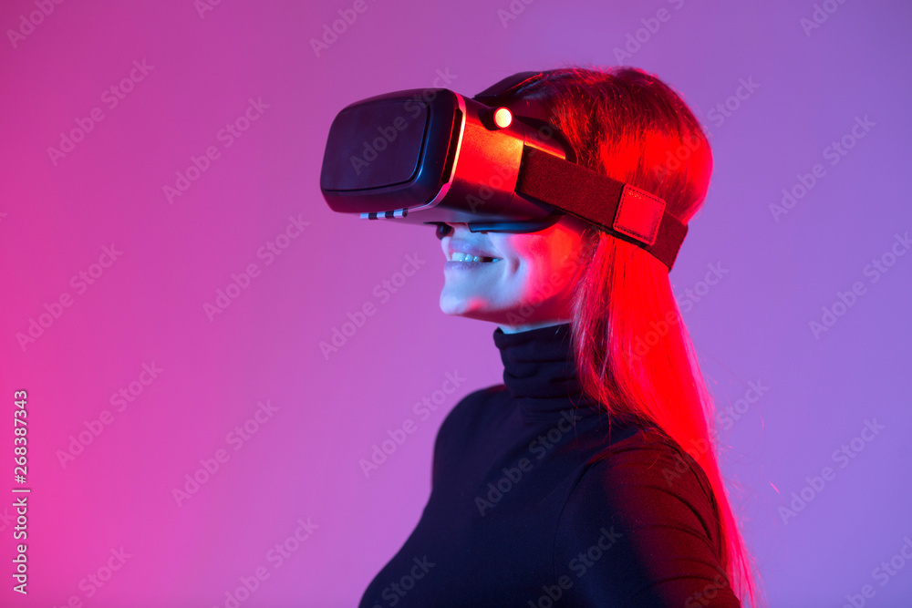 beautiful young girl wearing virtual reality glasses on a colored background