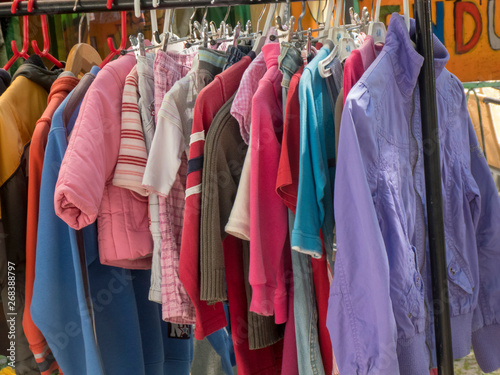 Colourful second-hand clothes and jackets hanging on a rack in a flea market