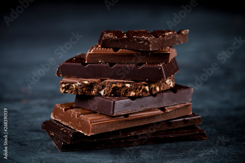 Chocolate bars pieces stack on black background. Sweet food photo concept.