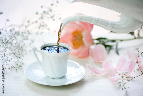 A cup of coffee and fresh flowers on a white table. photo