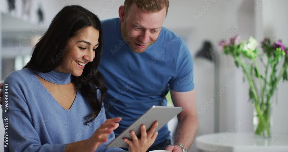 4K Couple relaxing at home, woman browsing the web & man bringing a cup of coffee. Slow motion.