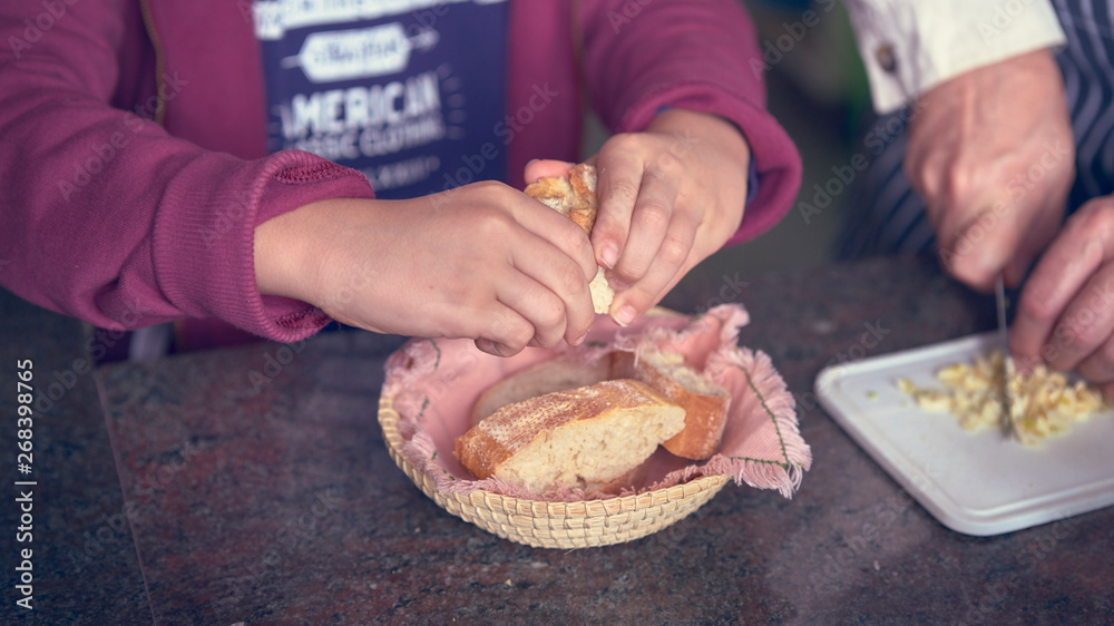 Photograph of a child holding bread while his family cooks. Huelva, España.