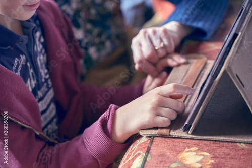 Photograph of the hands of a child and his grandmother using a tablet. Huelva, Spain