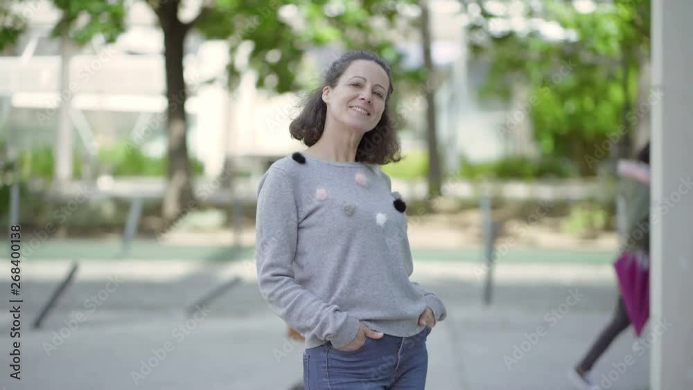Smiling beautiful middle aged woman posing outdoor. Attractive happy lady standing with hands in pockets on city street. Happiness concept Smiling beautiful middle aged woman posing outdoor. Attractive happy lady standing with hands in pockets on city street. Happiness concept