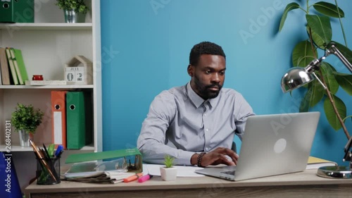 Attractive young Afro-American freelancer typing on his laptop at the light cozy and specious office. Modern technologies concept. Surfing the internet, browsing, social networks. Search engine. Male photo