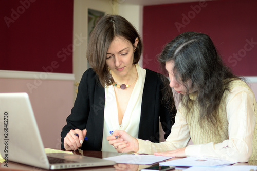 young smartly dressed lady helps another young lady to work with documents, fill forms and sign