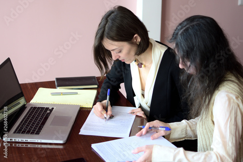 two young smartly dressed women filling out forms at a vintage office desk in front of a laptop