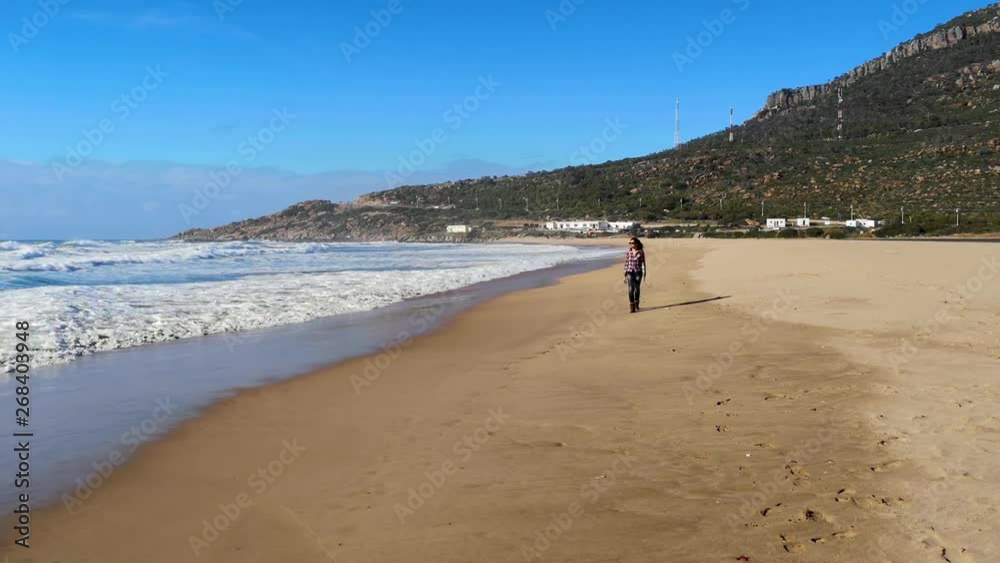 Brunette woman dressed walking on the Achakar beach in Tangier, Morocco Brunette woman dressed walking on the Achakar beach in Tangier, Morocco