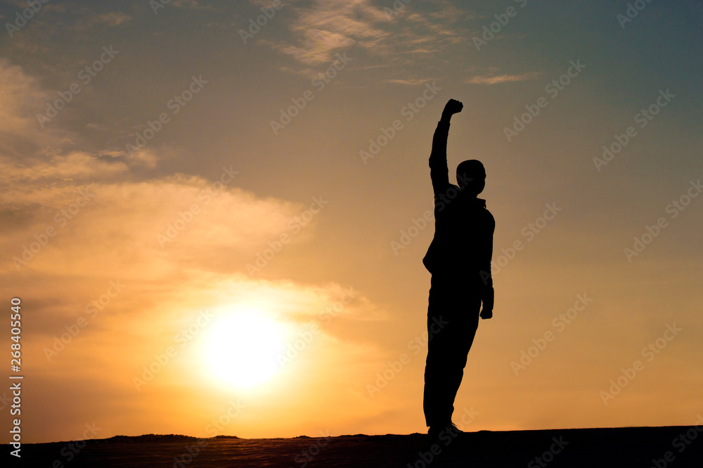 man walks with his hand raised at sunset