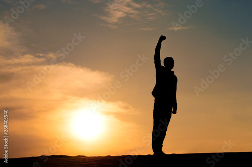 man walks with his hand raised at sunset