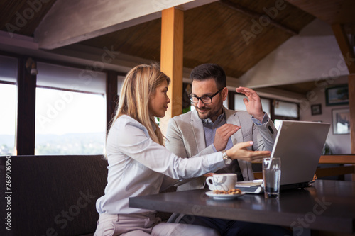 A handsome businessman explains the parts of the project to a beautiful blonde colleague while sitting in a restaurant in front of a laptop and drinking coffee.