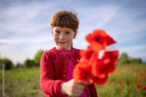 Bambina che offre dei papaveri rossi appena colti in uno sfondo di cielo azzurro con capelli riccioli biondi photo